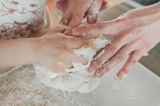 Hands of mother and daughter knead dough for pizza and bread. Having fun together in kitchen. Close-up.