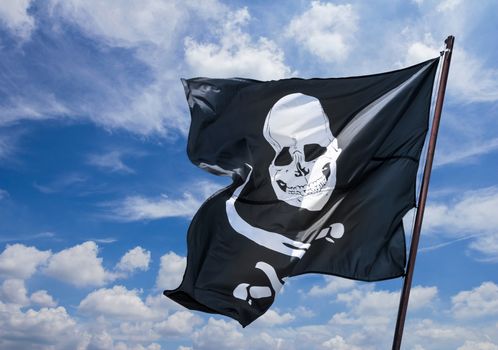 Pirates flag in the wind, depicting the skull and crossbones as a symbol of pirates. Pirate flag against blue sky. Space for text.