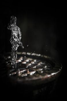 Water fountain jet creating a strange figure on dark background.