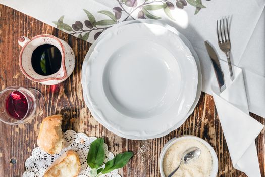 Traditional Italian table set with plate, cutlery, rustic bread, wine, parmesan. Flat lay. Copy space.