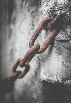 Rusty chain in the cement. Rusty chain anchored to the cement pole. Defocused blurry background. Retro style photo.