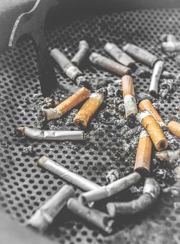Smoky ashtray. Smoked cigarettes butts in a dirty ashtray. Unhealthy life concept. Retro style photo.