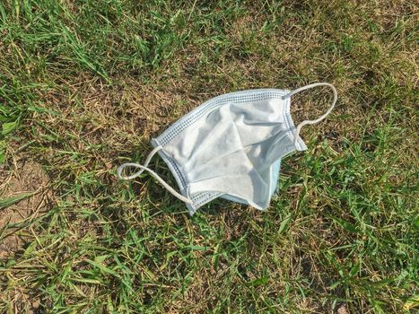 Disposable medical mask thrown on the street in the grass. The concept of environmental pollution after the coronavirus pandemic.