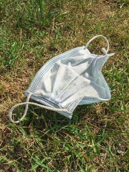 Disposable medical mask thrown on the street in the grass. The concept of environmental pollution after the coronavirus pandemic.