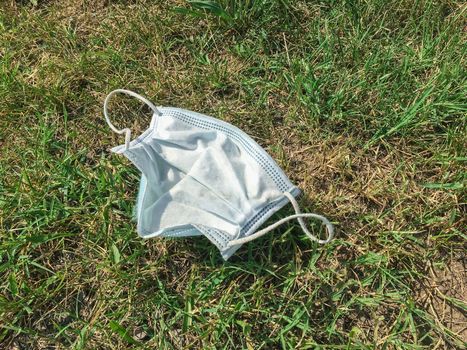 Disposable medical mask thrown on the street in the grass. The concept of environmental pollution after the coronavirus pandemic.