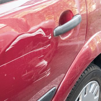 Scratched and dented car. Collision or accident. Scratches on the side door of the red car.