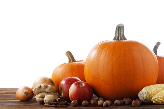 Autumn harvest still life with pumpkins, apples, hazelnut, corn, ginger, onion and cinnamon on wooden table isolated on white background