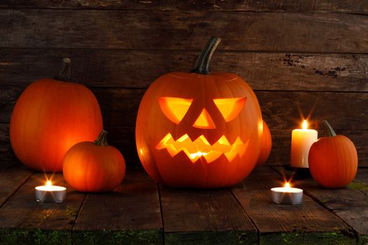 Halloween pumpkin head jack o lantern and candles on wooden background