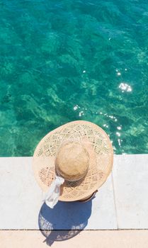 Graphic image of top down view of woman wearing big summer sun hat relaxing on pier by clear turquoise sea.