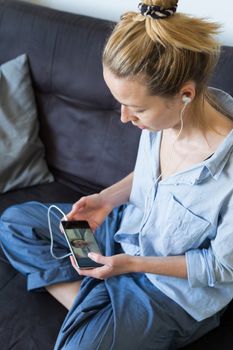 Stay at home, social distancing lifestyle. Woman at home relaxing on sofa couch using social media on phone for video chatting with her loved ones during corona virus pandemic.