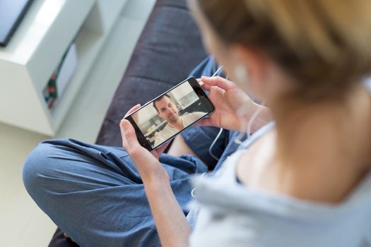 Stay at home, social distancing lifestyle. Woman at home relaxing on sofa couch using social media on phone for video chatting with her loved ones during corona virus pandemic.