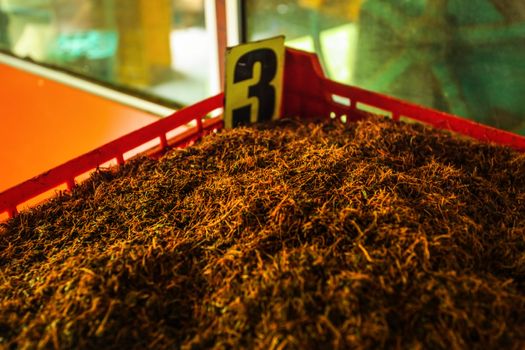 Detail of bulk Ceylon tea (orange pekoe leaves being dried) in plastic box labeled number 3, with green scenery behind windows. Kadugannawa Tea Factory, Kandy, Sri Lanka