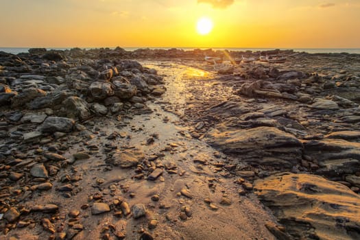 Rocks and beach uncovered in low tide with boats on dry land in background during evening sunset back light. Koh Lanta, Thailand