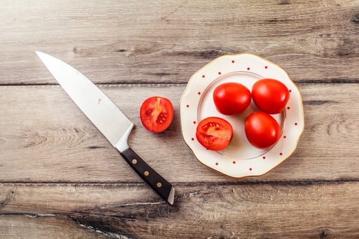 Tabletop photo of tomatoes, one of them cut, on a plate, with chef's knife on a wooden table.