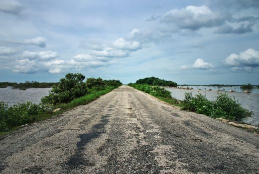 Old asphalt road leading through swamps with cloudy sky in background. Chelem, Mexico