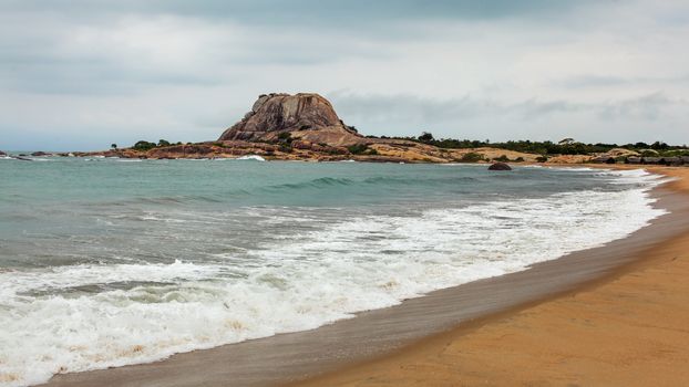 Beach with single hill (Patanangala rock) in distance on overcast day. Yala National Park, Sri Lanka