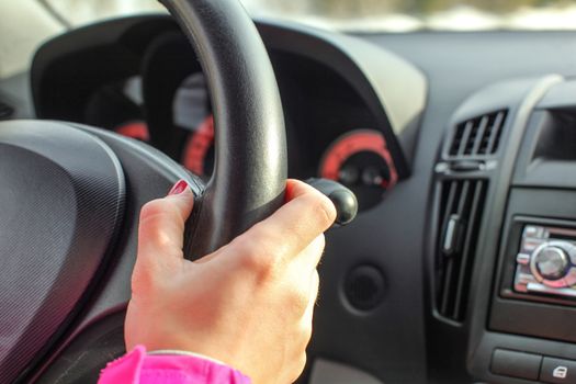 Detail on woman hand on leather car steering wheel while driving.