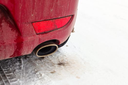 Detail on exhaust pipe of a red car parked on snow covered road.