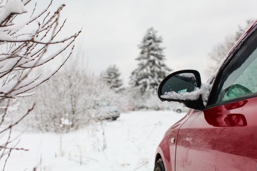 Detail on mirror of red car parked on a winter road with snow covered landscape in background.