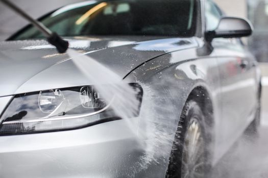 Detail on car front being washed with jet water in carwash.