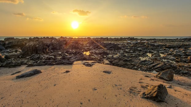 Rocks and sandy beach uncovered in low tide with boats on dry land in background during evening sunset light. Koh Lanta, Thailand