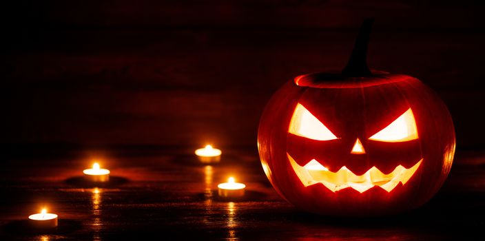 Halloween pumpkin head jack o lantern and candles on wooden background