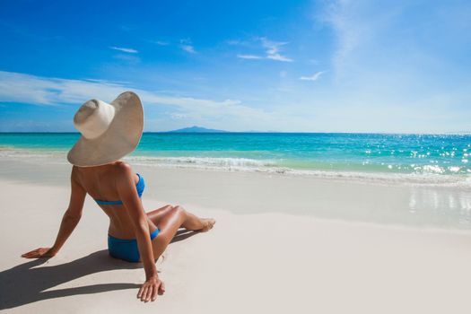 Beautiful tan woman in bikini lies on white sand beach looking on the sea, back view