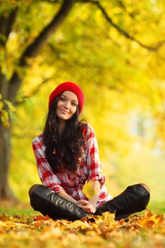 autumn woman portrait in park, young female sitting on ground with colorful maple leaves