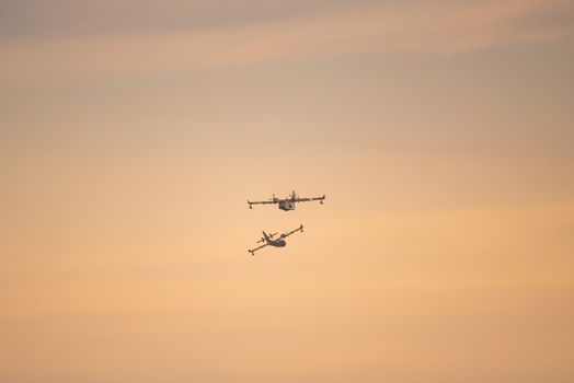 Two amphibious water bomber airplanes in flight at sunset, in France.