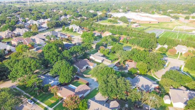 Residential neighborhood in school district with football field in background near Dallas, Texas, America. Suburban houses with large fenced backyard and large tree in early summer morning light