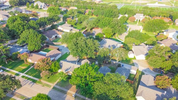 Drone view clean and empty neighborhood street with row of single family houses near Dallas, Texas, America. Suburban home with bungalow homes and large fenced backyard in early summer morning