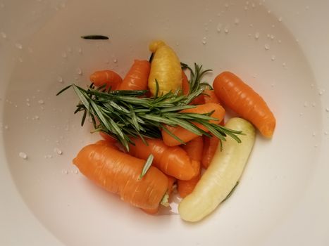 orange carrots and rosemary in white container or bowl