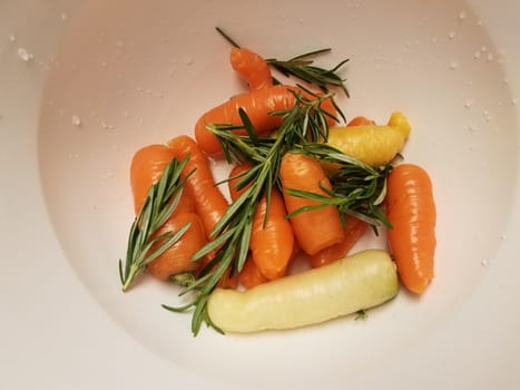 orange carrots and rosemary in white container or bowl