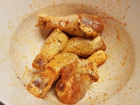 seasoned raw chicken drumsticks or poultry in white bowl