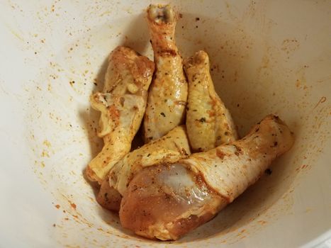 seasoned raw chicken drumsticks or poultry in white bowl