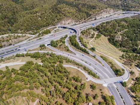 Day top panorama of European multi-level stack highway junction with passing cars through forest.