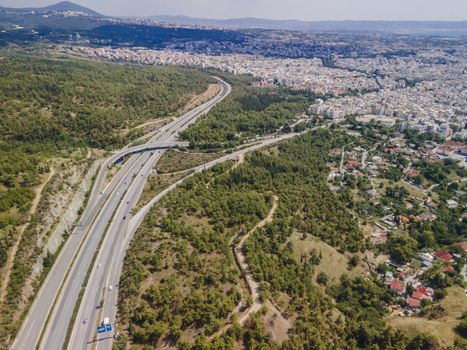 Day top panorama of European highway with passing cars through forest on city outskirts.