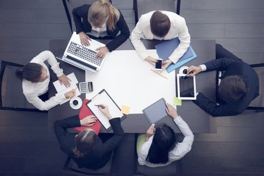 Business workplace with people, cup of coffee, digital tablet, smartphone, papers and various office objects on table