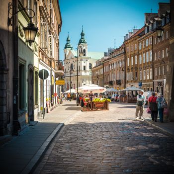 Warsaw, Poland - May 17, 2013. People walking in old and narrow cobblestone street of Warsaw, Poland, Europe. Beautiful sunny day, old church in background. Unesco world heritage sight.