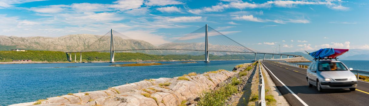 Panorama of car on road in Norway, Europe. Auto travel through scandinavia. Blue cloudy sky, lake and bridge in background.