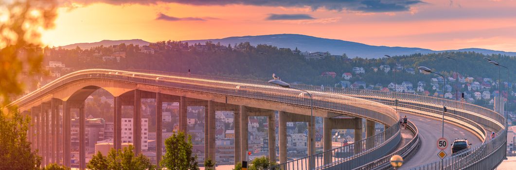 Panorama of bridge in Tromso and car road in Norway, Europe. Auto travel through scandinavia. Sunset with mountain and clouds in background.