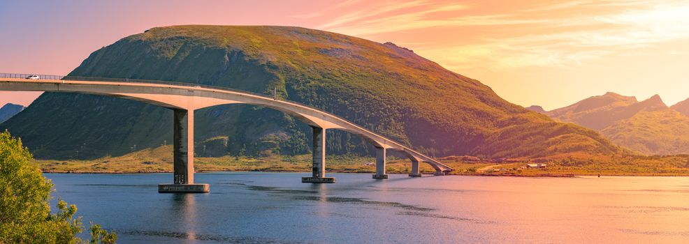 Panorama of bridge and car road in Norway, Europe. Auto travel through scandinavia. Sunset with mountain and clouds in background.