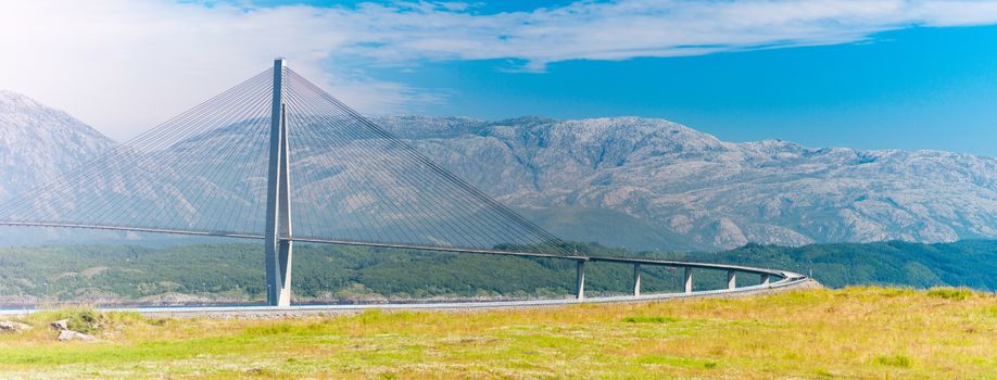 Panorama of bridge and car road in Norway, Europe. Auto travel through scandinavia. Blue cloudy sky and mountain in background.