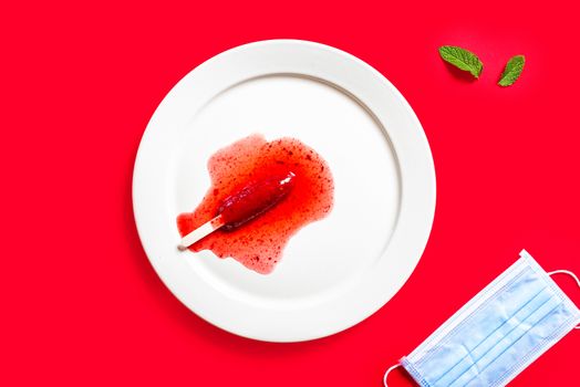 Delicious defrosted strawberry popsicles and medical mask over red background