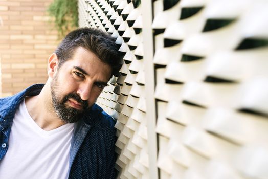 Thoughtful bearded male leaning on wall with hand on chin