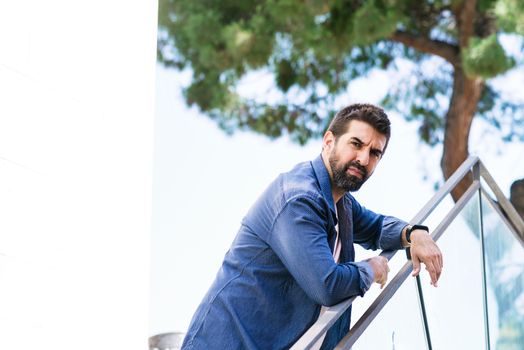 Bearded male leaning on fence while looking camera