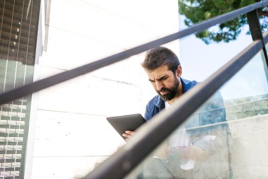 Portrait of a bearded man sitting on steps while using a tablet