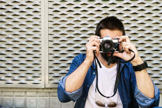 Cheerful bearded traveler man sitting on ground while using checking a camera