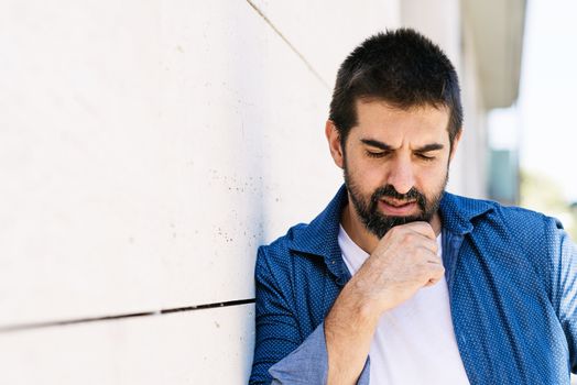 Thoughtful bearded male leaning on wall with hand on chin
