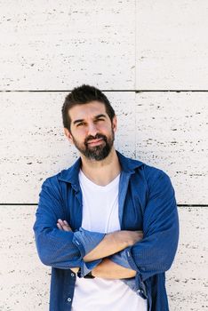 Bearded male leaning on wall with crossed arms while looking camera with a smile